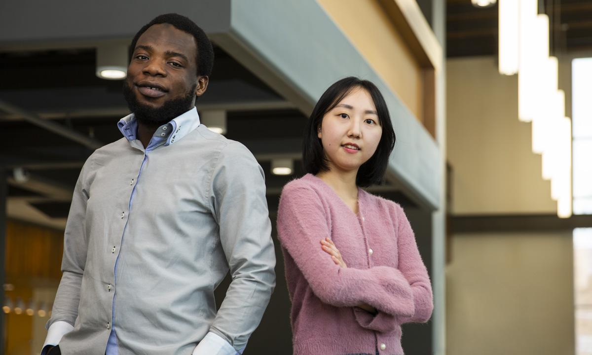 照片中，一位大学女生站在一位大学男生旁边，两人都微笑着看着镜头. 