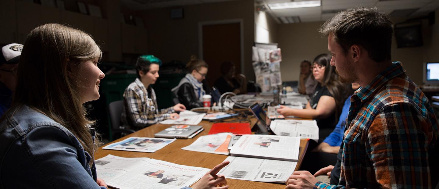 group of students sitting around a table covered with open newspapers