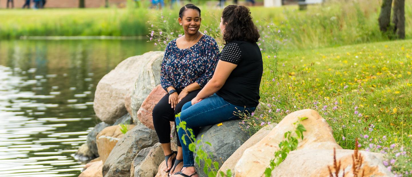 两个女人坐在韦德体育app官网池塘边的岩石上.