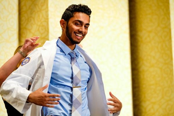 A student has help putting on his white coat on stage at the White Coat Ceremony. 