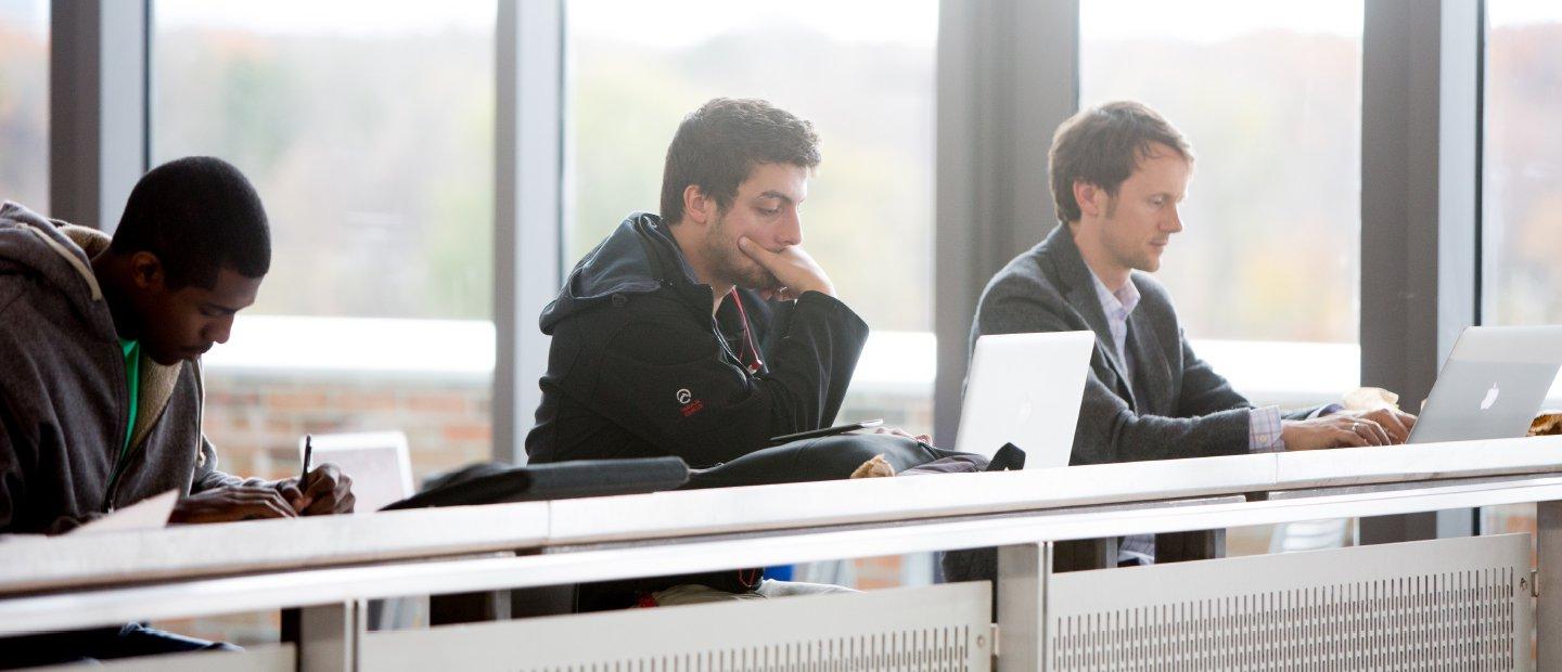 三个学生坐在一张放着笔记本电脑的长桌旁
